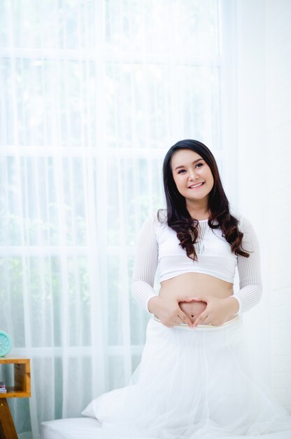 The maternity is enjoying the baby in the belly in a white dress and a white room.