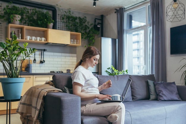 Congedo di maternità lavoro donna freelance incinta seduta a casa sul divano con laptop in abiti domestici funziona sul computer