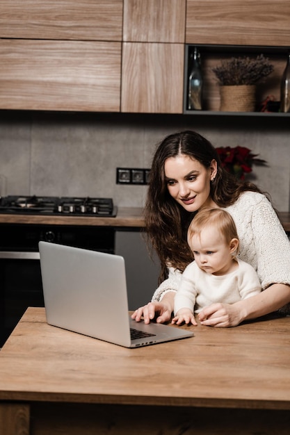 Maternity leave for young mother Happy family time with daughter at home Modern childhood Mom is sitting with toddler child and working on laptop remotely