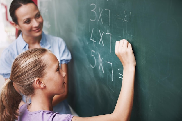 Math teacher and student writing on chalkboard in classroom for solving number problem and answer question Lesson girl and solution for multiplication at school with scholarship quiz and learning