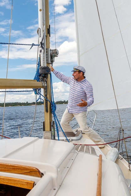 Matroos man in een pet op een boot onder zeil tegen de lucht en het water