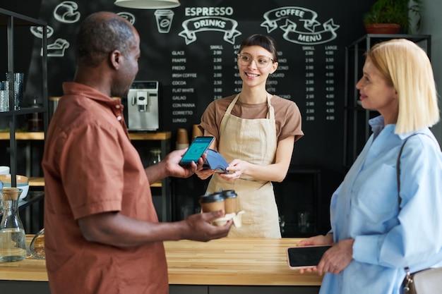 Mature African American man paying for coffee by smartphone in cafe