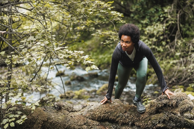 Mature African American woman hiker crossing a rock while exploring in the mountains and enjoying outdoor training.