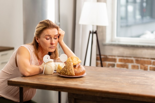 Mature appealing woman feeling hungry looking at bread and buns but having allergy