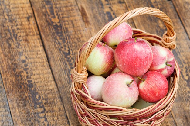 Mature apples with water drops in wicker basket on wooden boards. Shallow depth of field, Top view.