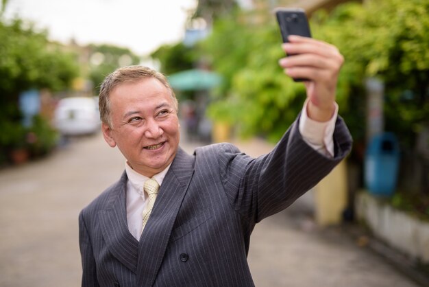 Зрелый азиатский бизнесмен с помощью мобильного телефона на улицах превзойти