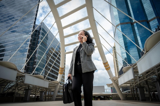 A mature Asian businesswoman is talking on the phone while commuting to work walking in the city