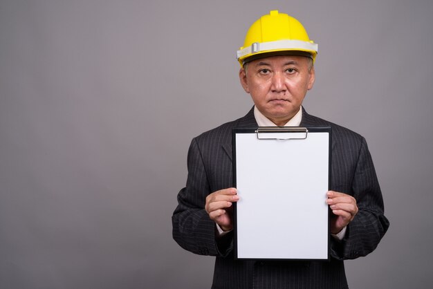 Mature Asian construction businessman against gray wall