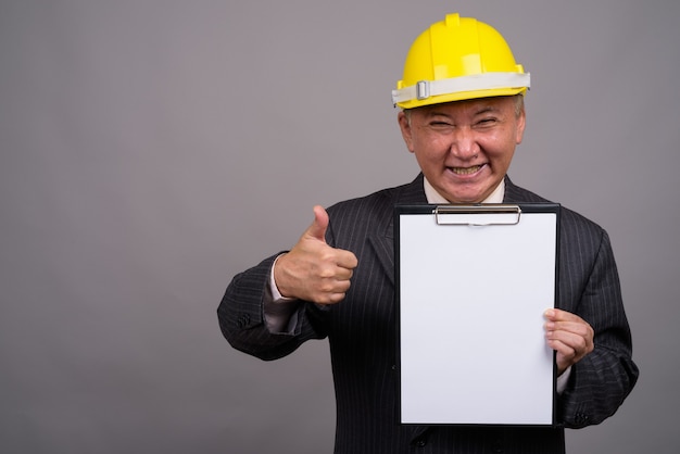 Mature Asian construction businessman against gray wall