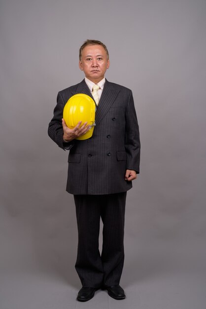 Mature Asian construction businessman against gray wall