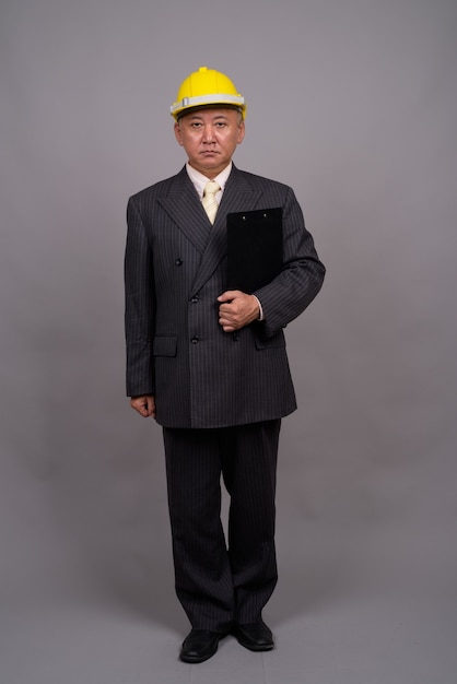 Mature Asian construction businessman against gray wall