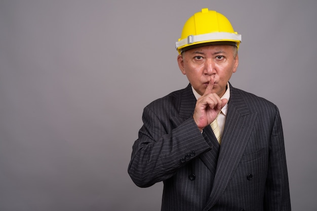 Mature Asian construction businessman against gray wall