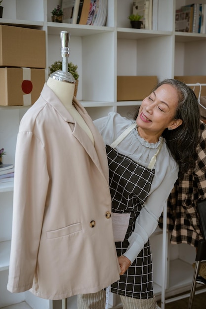 A mature Asian female tailor measuring a suit on a mannequin with a measuring tape