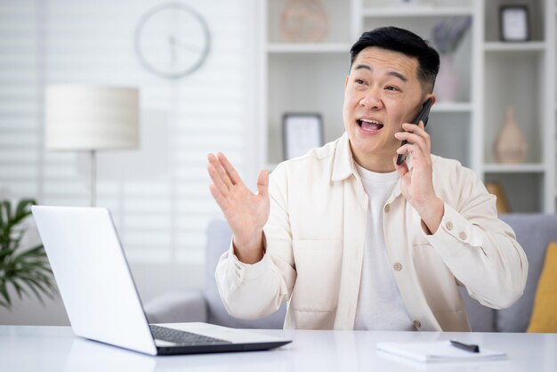 Mature asian man talking on the phone at home man working in home office sitting at desk in home