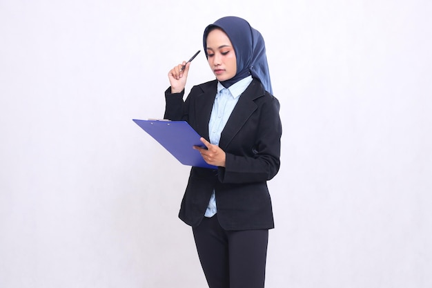Mature Asian office girl wearing a hijab stands elegantly thinking while holding up a pen and carryi