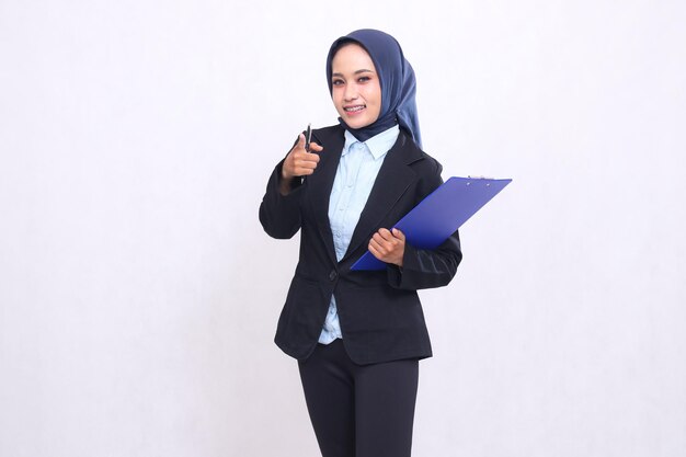 mature Asian office woman wearing a hijab standing smiling cheerfully pointing at you looking at the