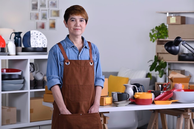 Mature Asian woman entrepreneur/ Business owner standing in front of her clay ceramic product and working at home