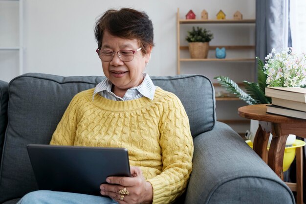 집에 앉아 디지털 태블릿을 사용하여 성숙한 아시아 여자
