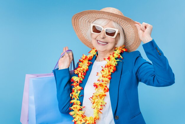 Mature attractive woman traveler enjoying shopping with bags in hand over blue background