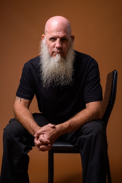 Mature bald man with long gray beard on brown