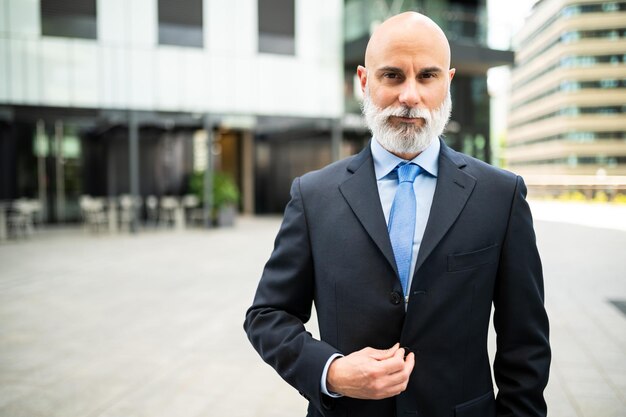Портрет зрелого лысого стильного бизнесмена с белой бородой на открытом воздухе