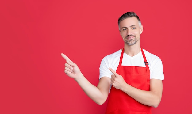 Mature barista in apron on red background point finger