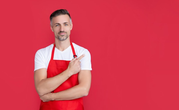 Mature barista in apron on red background pointing finger