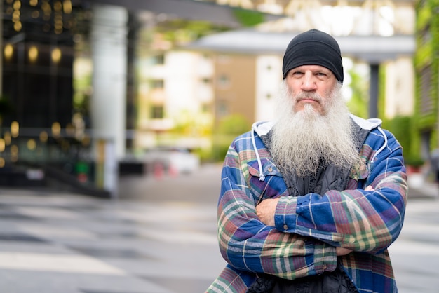 Mature bearded hipster man with arms crossed in the city streets outdoors