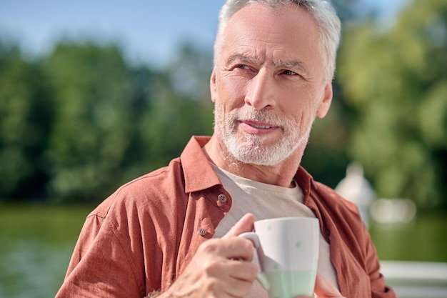 手にカップを持つ成熟したひげを生やした男