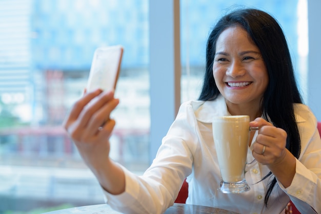 Mature beautiful Asian businesswoman relaxing inside the coffee