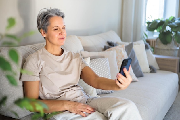 Mature beautiful middleaged woman with gray hair and poor eyesight sits on the couch