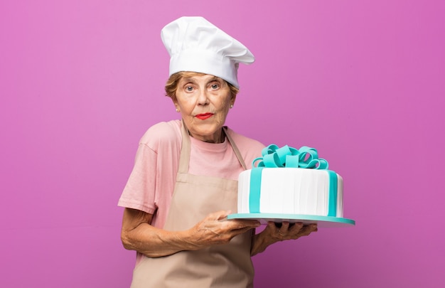 Bella vecchia donna matura che scrolla le spalle, sentendosi confusa e incerta, dubbiosa con le braccia incrociate e lo sguardo perplesso