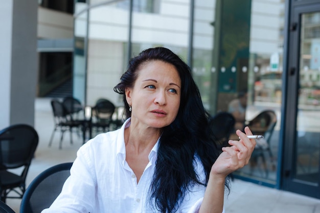 Mature beautiful woman sitting at a street cafeteria and smoking cigarette