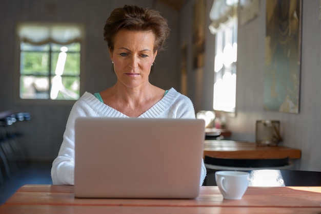 Mature beautiful woman with short hair using laptop inside coffee shop