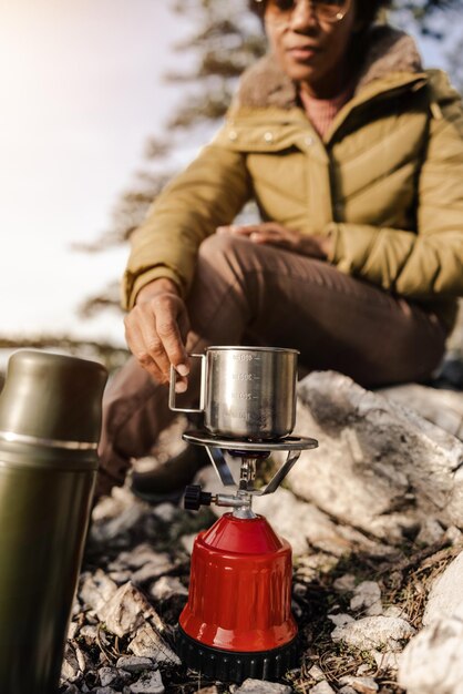 成熟した黒人女性が丘の上に座って、山でのハイキング中にお茶を飲んでいます。