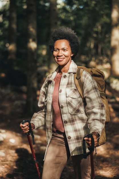 Mature black woman with backpack and trekking poles hiking alone in mountains.