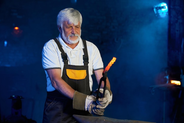 Mature blacksmith working with heated steel on anvil