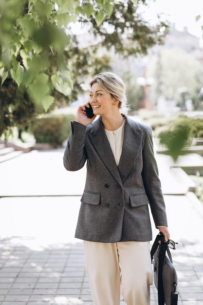 Mature blond smiling business woman walks the city streets and speaks on the phone