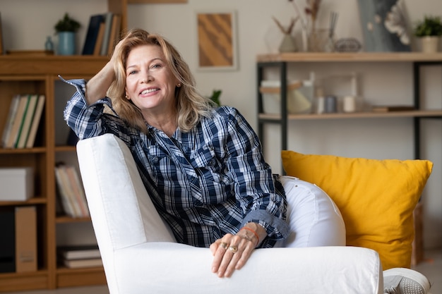 Mature blond woman with toothy smile sitting in comfortable white leather armchair