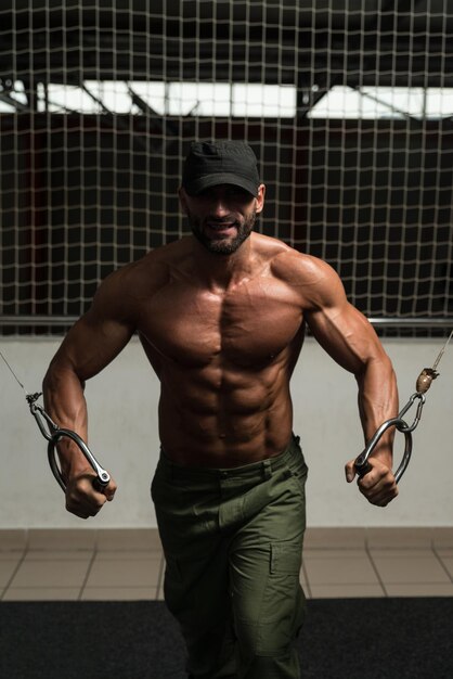 Photo mature bodybuilder is working on his chest with cable crossover in a dark gym
