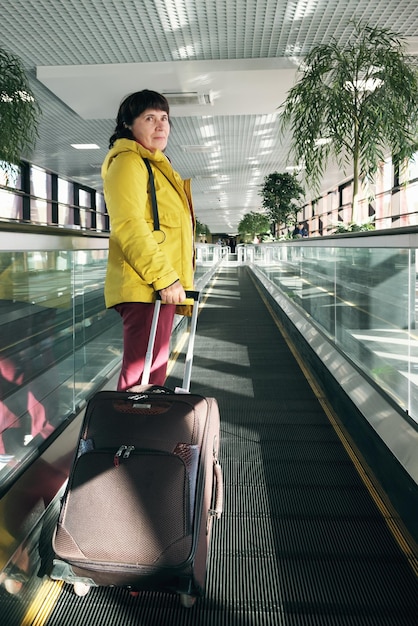 Photo mature brunette woman at the airport stands on a moving walkway