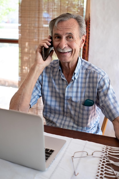 Mature business man smiling and talking on phone in front of laptop looking towards camera