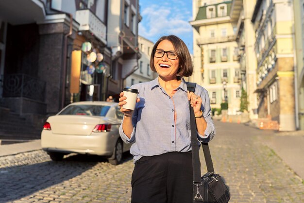 Mature business woman in glasses with office laptop bag walking along city street