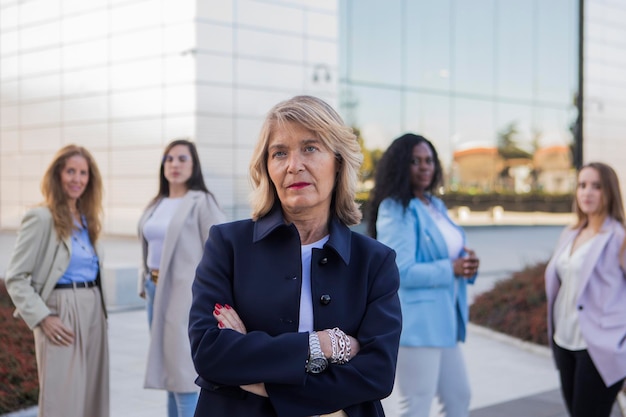 Mature Business woman looking at the camera with her arms crossed while standing in front of her business team outdoors Business concept