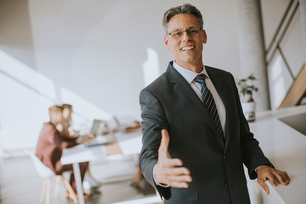 Mature businessman approaching  and offering for hand for handshake in office