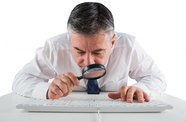 Mature businessman examining with magnifying glass on white background