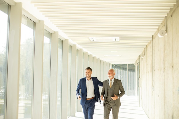 Mature businessman and his young colleague discussing financial report in the office corridor