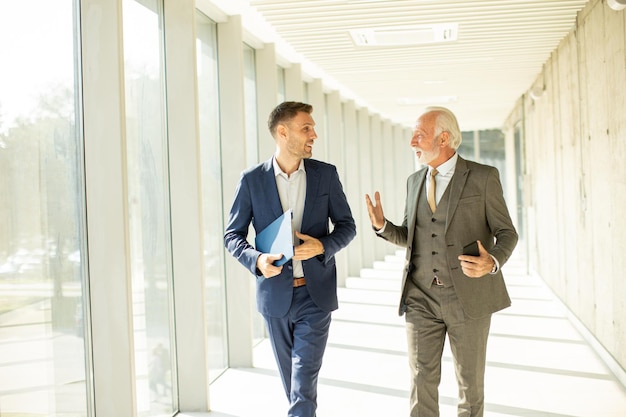 Mature businessman and his young colleague discussing financial report in the office corridor