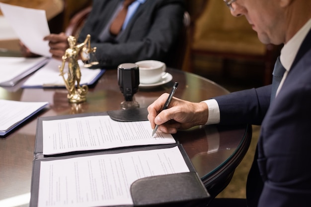 Photo mature businessman or jurist signing document by workplace