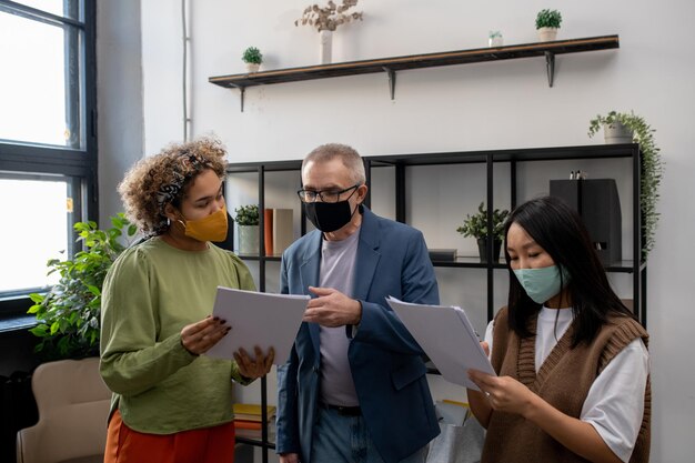 Mature businessman in mask pointing at document during discussion